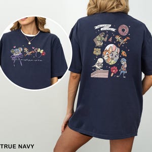 May include: Navy blue t-shirt with a vibrant cartoon graphic and the words "You can be anything you wish to be." The design includes a donut, badge, and animal characters. The shirt is a relaxed fit, perfect for casual wear.