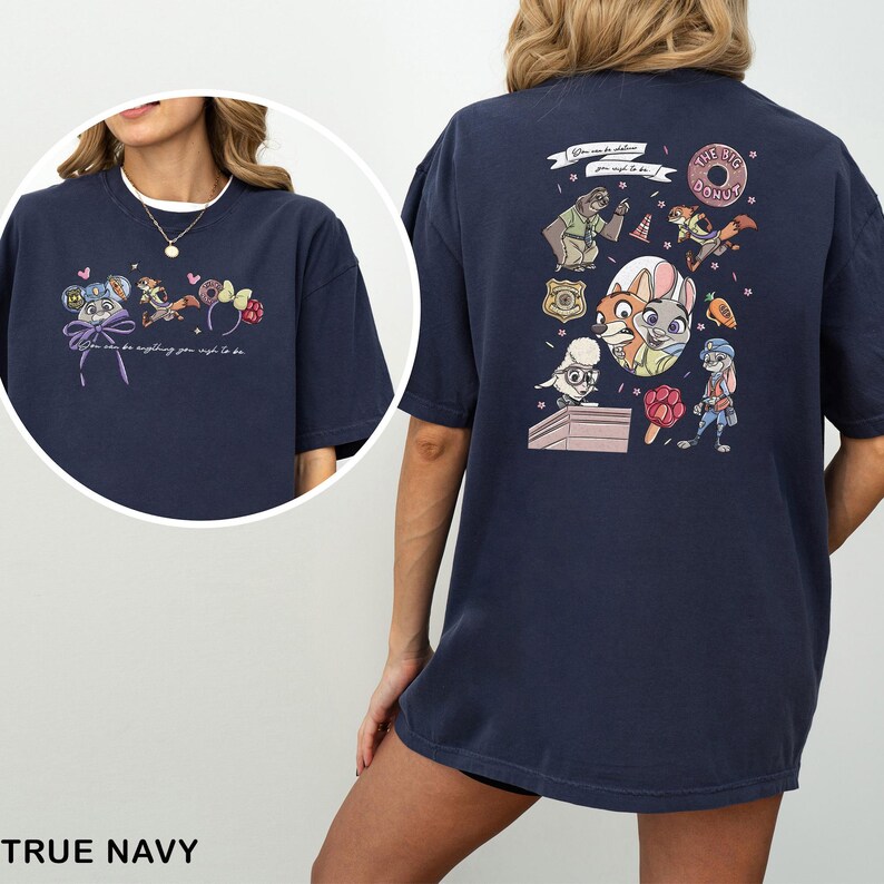 May include: Navy blue t-shirt with a vibrant cartoon graphic and the words "You can be anything you wish to be." The design includes a donut, badge, and animal characters. The shirt is a relaxed fit, perfect for casual wear.