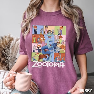 May include: Berry-colored t-shirt featuring a colorful graphic from the animated film "Zootopia." The design includes various characters from the movie in a grid layout, with the film's title in white block letters at the bottom.