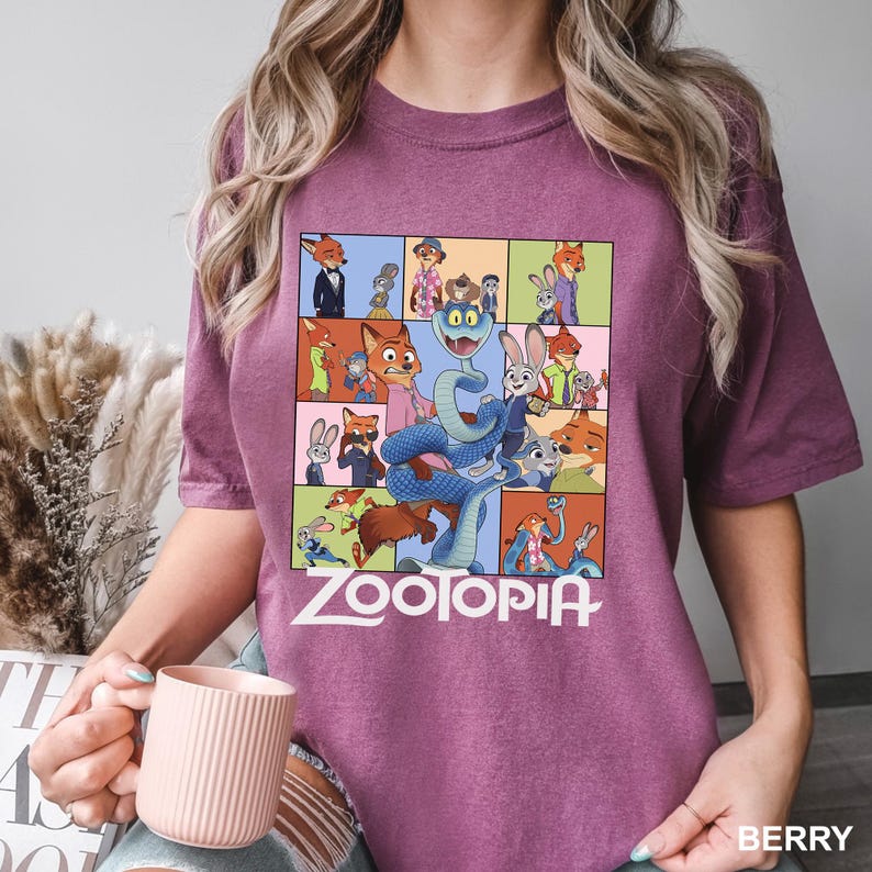 May include: Berry-colored t-shirt featuring a colorful graphic from the animated film "Zootopia." The design includes various characters from the movie in a grid layout, with the film's title in white block letters at the bottom.