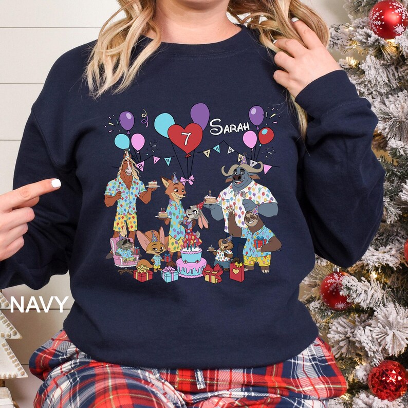 May include: Navy blue sweatshirt featuring a colorful cartoon illustration of Zootopia characters celebrating a birthday. The design includes balloons, a cake, and the name "Sarah" with the number "7". The word "NAVY" is printed on the bottom left.