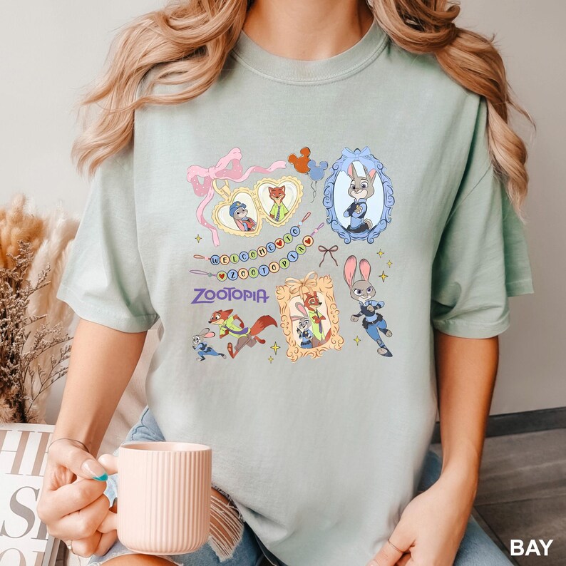 Op de afbeelding: Lichtgroen T-shirt met cartoonfiguren uit de film Zootopia. Het ontwerp bevat ingelijste portretten van de personages, het woord "Zootopia" en de zin "Welcome to Zootopia".