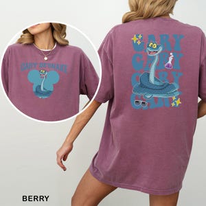 May include: Berry-coloured t-shirt with a cartoon snake design. The front of the shirt displays the text "GARY DE'SNAKE" above a snake illustration. The back of the shirt has a larger snake graphic with the text "GARY" repeated three times.