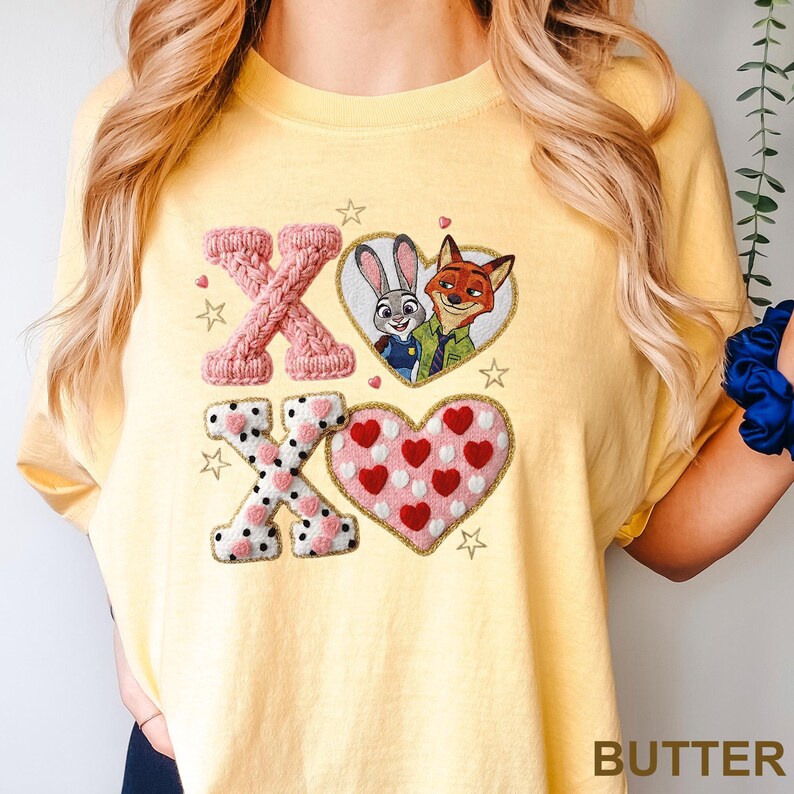 May include: A pale yellow t-shirt featuring a graphic design with the letters X and O in a textured pink knit pattern, a second X and O in a white and black polka dot pattern, a heart with Judy Hopps and Nick Wilde, and a heart with red hearts.