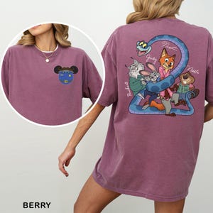 May include: Berry-colored t-shirt featuring a cartoon graphic on the front and back. The front graphic is a blue and yellow cartoon character. The back graphic features cartoon characters and the text "Judy", "Nick", and "Nibbles".