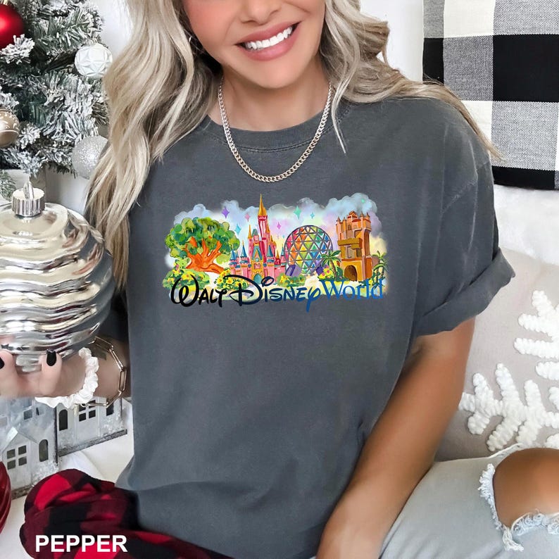 May include: A charcoal gray short-sleeve t-shirt featuring a colorful graphic print of Walt Disney World landmarks, including a tree, a pink castle, a geodesic dome, and a tower, with the text Walt Disney World printed in blue cursive script.
