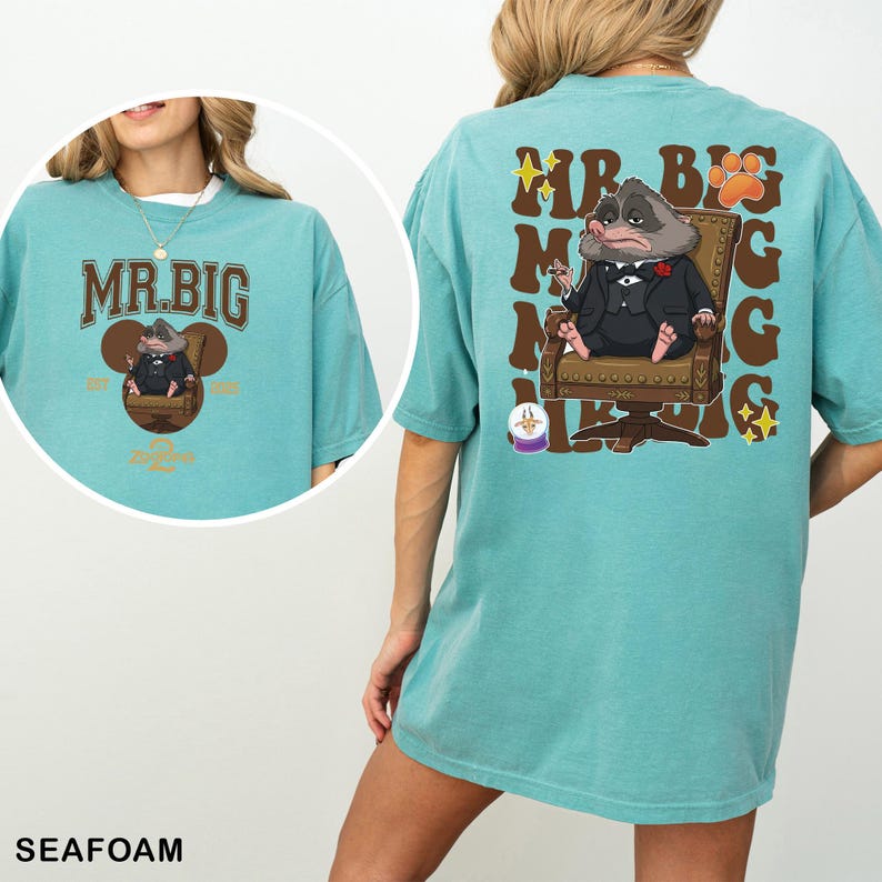 May include: Seafoam green t-shirt with a cartoon illustration of a rodent in a suit seated in a chair. The front of the shirt has the text "MR. BIG" in brown lettering. The back of the shirt has the same illustration and text.