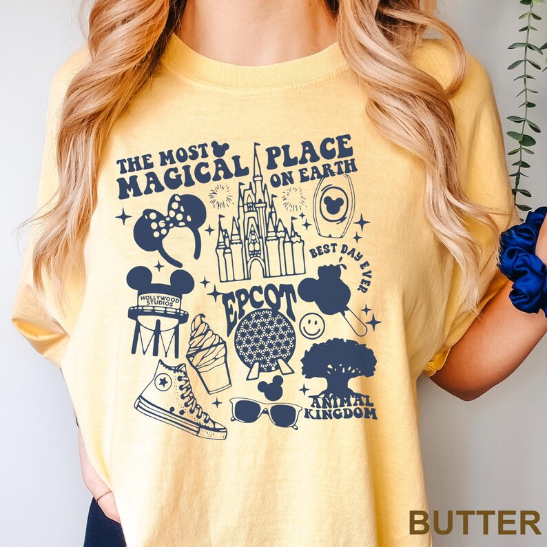 Puede incluir: Camiseta de color mantequilla con un dise&ntilde;o gr&aacute;fico azul marino. El dise&ntilde;o incluye el texto "The Most Magical Place on Earth" e iconos de Disney como un castillo y orejas de Mickey Mouse.