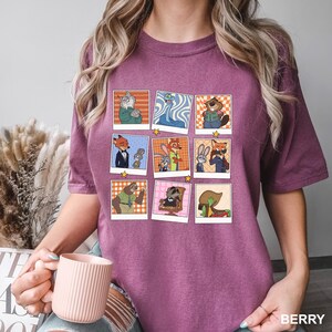 May include: Berry-colored t-shirt featuring a grid of cartoon character portraits. Each portrait is framed with a white border and a yellow star. The shirt's color is labeled "BERRY" at the bottom right.