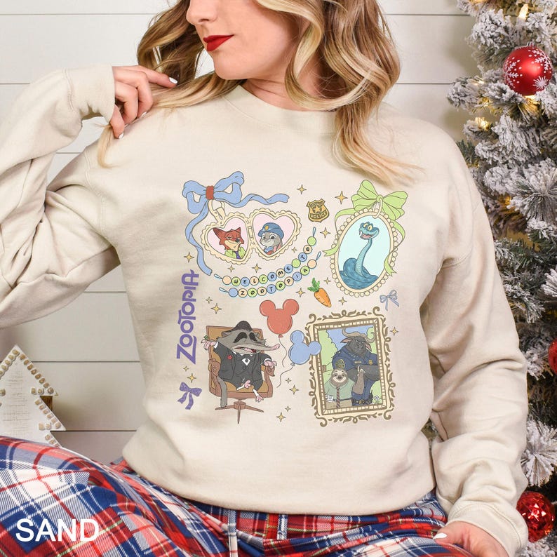 以下が含まれることがあります： アニメ映画「ズートピア」のキャラクターのイラストが額縁に入った、サンドカラーのスウェットシャツ。キツネ、ウサギ、ナマケモノ、アライグマのデザインで、左側には「ズートピア」の文字が縦にプリントされています。