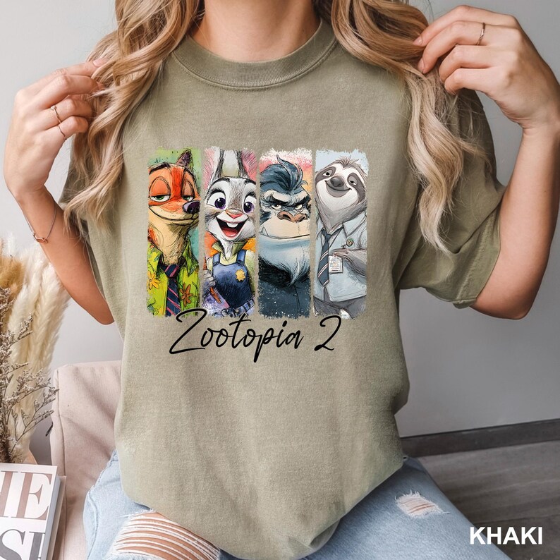 Peut inclure: T-shirt kaki avec un graphisme color&eacute; des personnages de Zootopie 2 : Nick Wilde, Judy Hopps, Duke Weaselton et Flash. Les mots "Zootopia 2" sont &eacute;crits en cursive en dessous des personnages.
