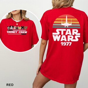 May include: Red t-shirt with a Disney Crew design on the front and a Star Wars graphic on the back. The front design shows Disney characters and the text "DISNEY CREW". The back design features the text "STAR WARS 1977".
