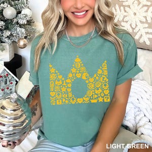 May include: Light green t-shirt with a yellow crown design made of various video game icons. The text "LIGHT GREEN" is at the bottom of the image. The shirt is a solid color and has rolled-up sleeves.
