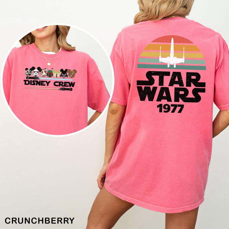 May include: A pink t-shirt with a Disney Crew graphic on the front and a Star Wars design on the back. The Star Wars design includes a sunset, a spaceship, and the text "STAR WARS 1977".
