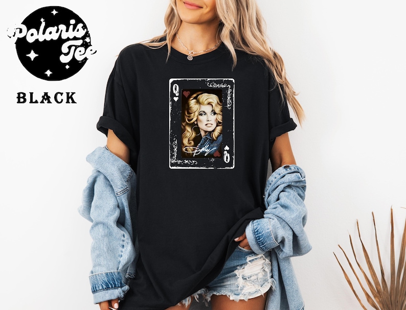 May include: A black t-shirt featuring a graphic print of a playing card with the letter Q and a heart symbol. The card displays a portrait of a blonde person with wavy hair, wearing a denim jacket, with the name Dolly written in white script below.