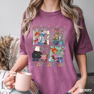 K&ouml;nnte beinhalten: Beerenfarbenes T-Shirt mit einer farbenfrohen Grafik von Charakteren aus einem beliebten Zeichentrickfilm. Die Grafik ist in vier Quadrate mit verschiedenen Zeichengruppierungen unterteilt. Das Shirt hat einen Rundhalsausschnitt und kurze &Auml;rmel.
