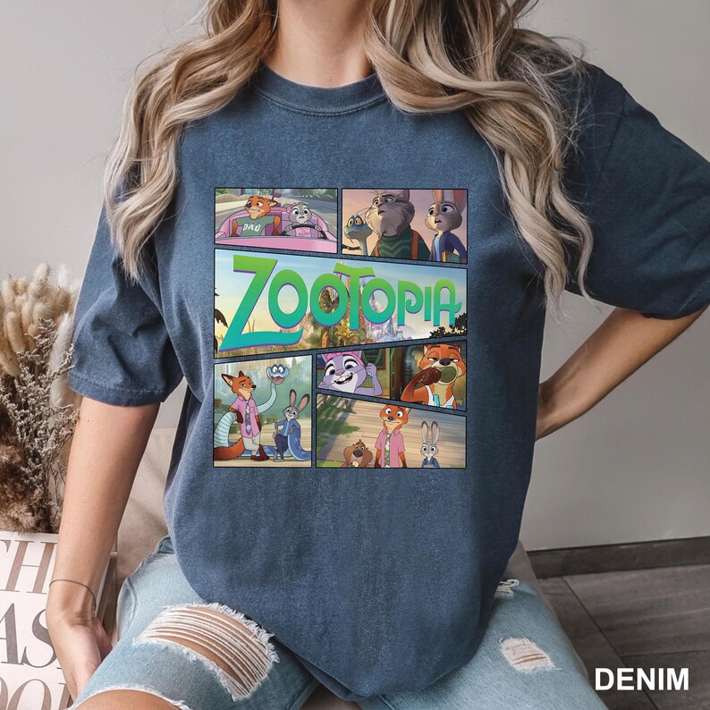 K&ouml;nnte beinhalten: Ein kurz&auml;rmeliges T-Shirt in Denim-Blau mit einem Grafikdruck verschiedener Szenen aus dem Film Zoomania. Das Design enth&auml;lt mehrere Felder mit Charakteren wie Nick Wilde und Judy Hopps sowie das Wort Zoomania in gro&szlig;en gr&uuml;nen Buchstaben.