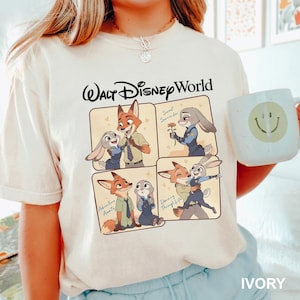 K&ouml;nnte beinhalten: Elfenbeinfarbenes T-Shirt mit einem Walt Disney World-Motiv. Die Grafik zeigt Cartoon-Bilder eines Fuchses und eines Kaninchens in verschiedenen Posen, mit Text wie "Sweet Surrender", "Adventure Awaits" und "Dancing Through Life".