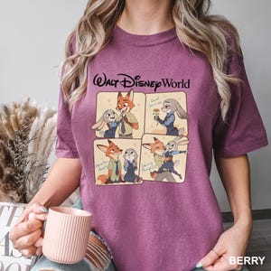 K&ouml;nnte beinhalten: Beerenfarbenes T-Shirt mit einer Grafik mit vier Panels von Zootopia-Charakteren, dar&uuml;ber der Text "Walt Disney World". Die Panels zeigen Nick Wilde und Judy Hopps in verschiedenen Posen. Das Wort "BERRY" ist unten rechts aufgedruckt.