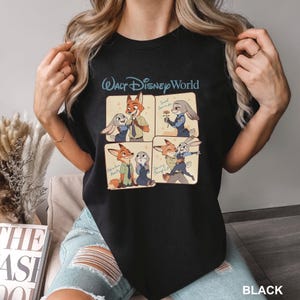 K&ouml;nnte beinhalten: Schwarzes T-Shirt mit einem viergeteilten Grafikdesign von Zootopia-Charakteren und dem Text "Walt Disney World" dar&uuml;ber. Die Panels zeigen Nick Wilde und Judy Hopps in verschiedenen Posen. Das Wort "BLACK" ist unten aufgedruckt.
