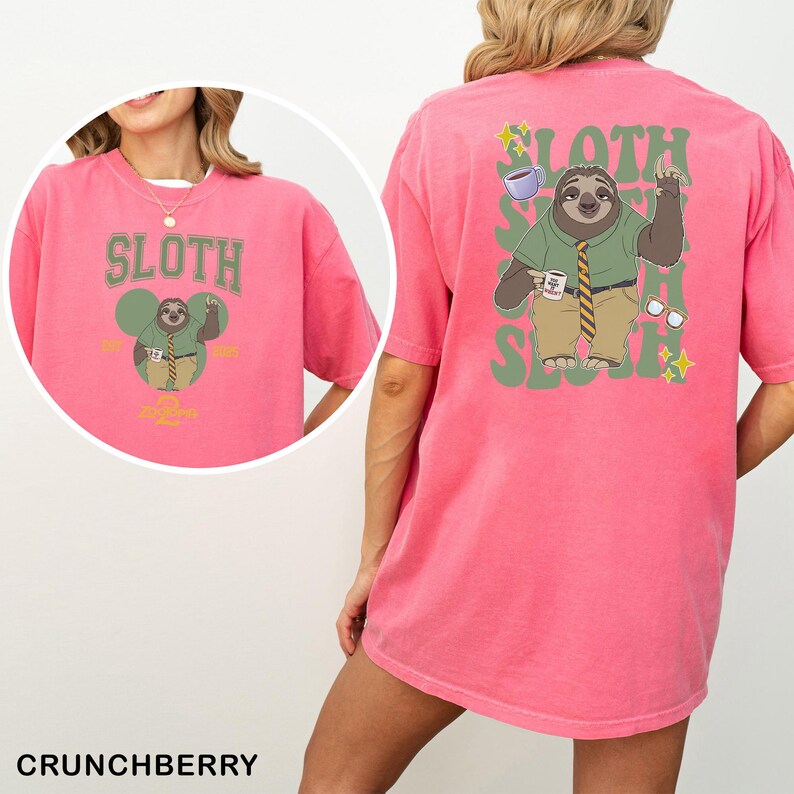 May include: A pink t-shirt featuring a sloth cartoon design. The front displays "SLOTH" above a sloth character with a coffee cup. The back has a larger sloth graphic with "SLOTH" and "SLOTH" in green. The shirt is a comfortable fit.