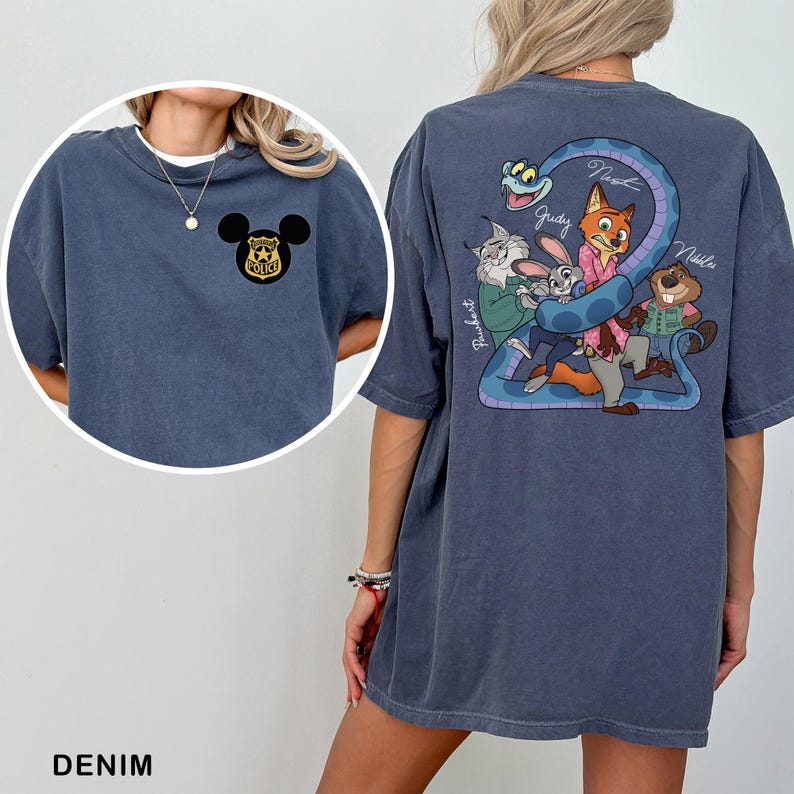 May include: Denim blue t-shirt featuring a Mickey Mouse police badge on the front and a cartoon graphic on the back. The graphic includes characters like Judy, Nick, and others, with the names of the characters written on the shirt.