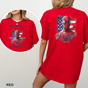 May include: A bright red t-shirt featuring a graphic of the superhero Spider-Man centered over a stylized American flag. The design includes the text UNITED STATES. The back of the shirt displays a larger version of the same graphic print.
