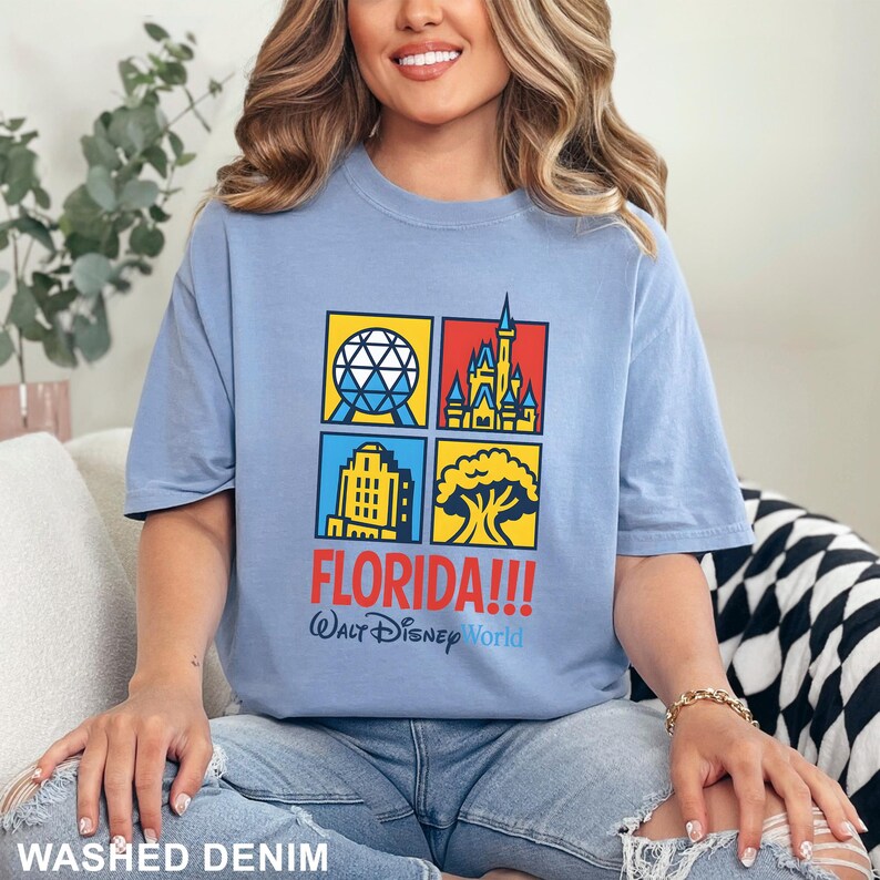 Może przedstawiać: Jasnoniebieska koszulka z kolorową grafiką przedstawiającą zabytki Florydy. Projekt zawiera napis "FLORIDA!!!" i "Walt Disney World". Koszulka wykonana jest z miękkiego materiału i oznaczona napisem "WASHED DENIM".