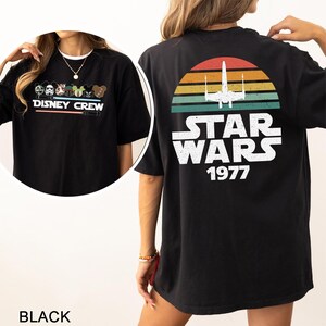May include: Black t-shirt with a Disney Crew design on the front and a Star Wars 1977 graphic on the back. The front design includes Disney characters and the text "DISNEY CREW". The back design features a retro sunset and a Star Wars logo.