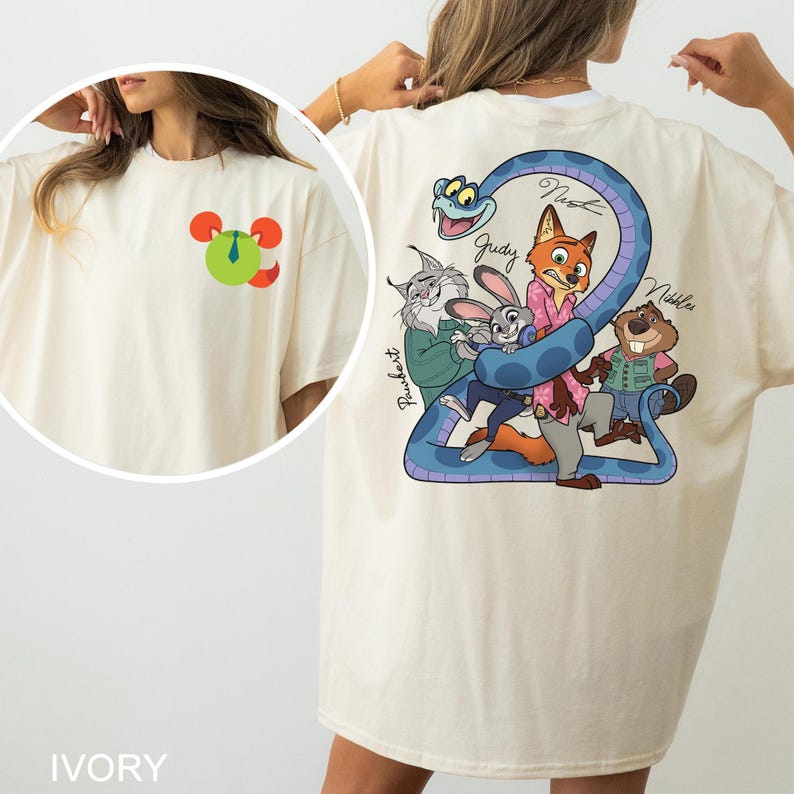 May include: Ivory-colored t-shirt featuring a cartoon graphic on the front and back. The back graphic includes a blue snake with cartoon characters and the names Judy, Nick, and Nibbles. The front has a Mickey Mouse-like design.