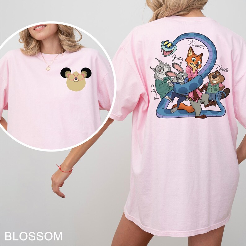 May include: Light pink t-shirt with a cartoon graphic on the front and back. The front features a mouse-like character, while the back displays a blue snake and cartoon characters. The word "Blossom" is at the bottom.