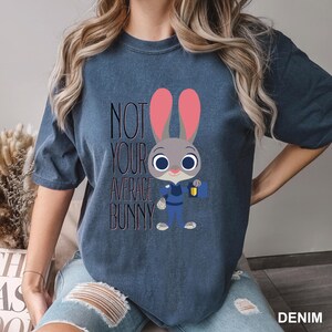 May include: Denim blue t-shirt featuring a cartoon bunny character with pink ears and a police uniform. The text "NOT YOUR AVERAGE BUNNY" is printed above the character. The shirt is a casual style.