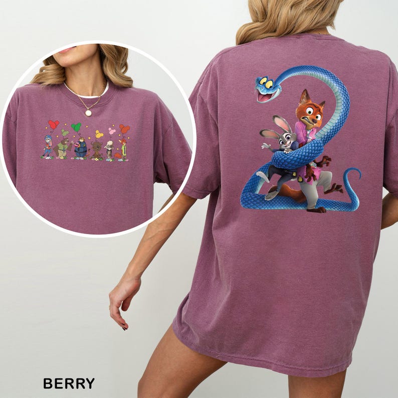 Op de afbeelding: Bessenkleurig T-shirt met een cartoonillustratie op de achterkant van een vos en een konijn die door een blauwe slang worden omarmd. De voorkant van de shirt heeft een kleinere illustratie van cartoonfiguren en harten.