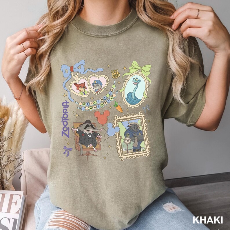 Puede incluir: Una camiseta color caqui con un estampado gr&aacute;fico de Zootopia que incluye personajes como Nick Wilde, Judy Hopps, Mr. Big, Flash y el Jefe Bogo en marcos ornamentados, junto a una placa de polic&iacute;a, una zanahoria y globos con forma de Mickey.