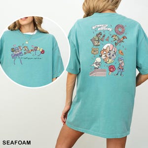 May include: Seafoam green t-shirt with cartoon characters and the text "You can be anything you might to be." The front has a cartoon design with a bow, mouse ears, and hearts. The back has a larger cartoon design.