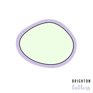 May include: A cookie cutter with a rounded, irregular shape. The cutter has a light green interior, a black outline, and a lavender border. The words "BRIGHTON Cutters" are in the lower right corner.