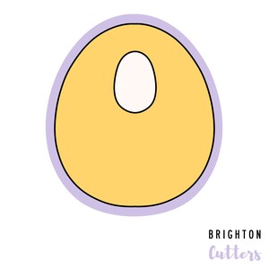 May include: A yellow cookie cutter shaped like an egg with a smaller circle cut out of the center. The cutter has a purple outline.