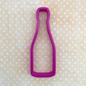 May include: A pink plastic cookie cutter shaped like a bottle of champagne.