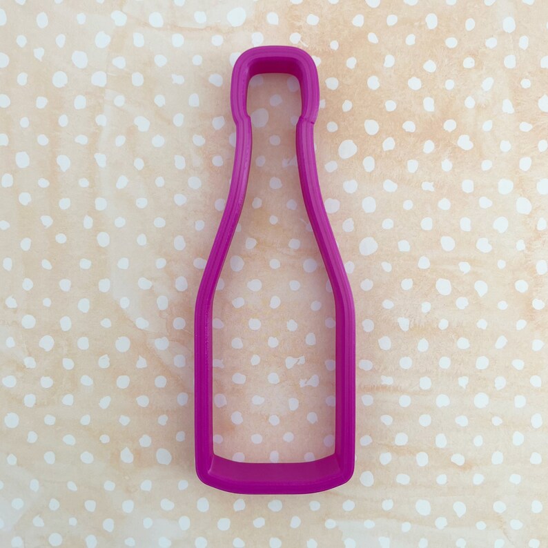 May include: A pink plastic cookie cutter shaped like a bottle of champagne.