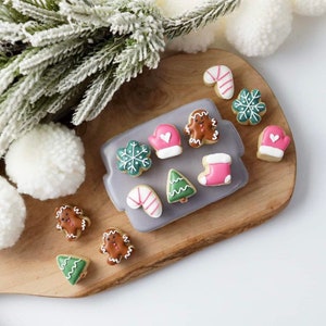 May include: A wooden board with a variety of Christmas-themed sugar cookies. The cookies are decorated with icing in various colors, including red, green, white, and brown. The cookies feature designs such as snowflakes, Christmas trees, candy canes, mittens, and gingerbread people.