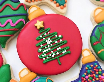 Könnte beinhalten: Sortiment von weihnachtlichen Zuckerplätzchen, verziert mit buntem Zuckerguss und Streuseln. Ein Plätzchen ist in Form eines roten Christbaumschmucks mit einem grünen Weihnachtsbaum und weißen Streuseln.