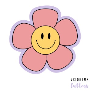 May include: A pink flower with a yellow smiley face in the center. The flower has six petals and is outlined in black. The background is white.