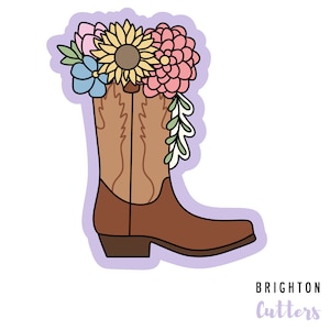 May include: A brown cowboy boot with a floral arrangement of sunflowers, pink and blue flowers, and green leaves in the top of the boot. The boot is outlined in black and the background is a light purple. The text "BRIGHTON Cutters" is at the bottom of the image.