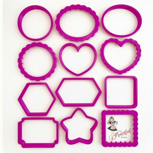 May include: A set of 12 pink plastic cookie cutters in various shapes, including circles, ovals, hearts, stars, squares, and rectangles. The cutters are arranged in two rows on a white surface.