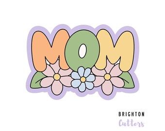 Könnte beinhalten: Ein bunter Ausstecher in Form des Wortes "MOM" mit drei Blumen darunter. Die Blumen sind rosa, blau und gelb. Der Ausstecher befindet sich auf einem hellvioletten Hintergrund.
