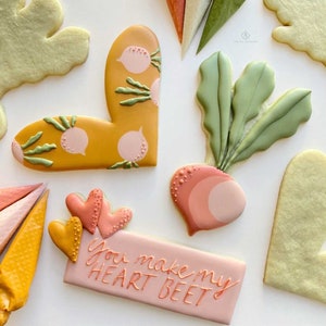 May include: A set of decorated sugar cookies with a beet, hearts, and a sign that reads "You make my heart beet".