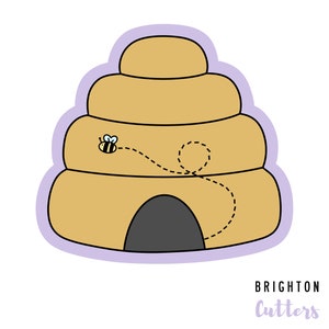May include: A tan, dome-shaped beehive cookie cutter with a light purple border. The design features a small yellow and black bee with blue wings and a dashed black flight path leading to a dark grey arched entrance. The text Brighton Cutters is visible.