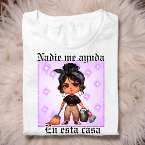 May include: White t-shirt featuring a cartoon illustration of a woman holding a broom and a bucket. The text "Nadie me ayuda en esta casa" is printed on the shirt.