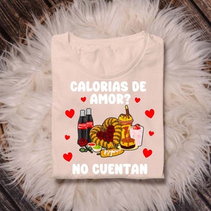 May include: A beige t-shirt with the text "Calorias de Amor? No Cuentan" in red and black. The design features a heart-shaped arrangement of various Mexican foods, including churros, corn on the cob, and a drink with a straw.