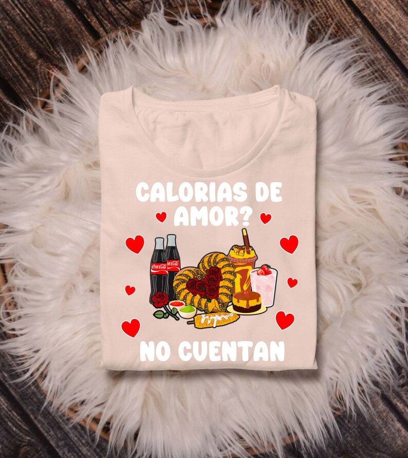 May include: A beige t-shirt with the text "Calorias de Amor? No Cuentan" in red and black. The design features a heart-shaped arrangement of various Mexican foods, including churros, corn on the cob, and a drink with a straw.